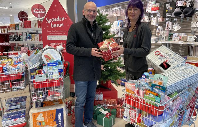 Zwei Personen in Rossmann übergeben Geschenk an Wunschbaum-Aktion