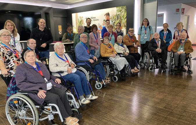 Gruppe älterer Menschen im Rollstuhl mit Betreuungspersonal bei Firmenbesuch