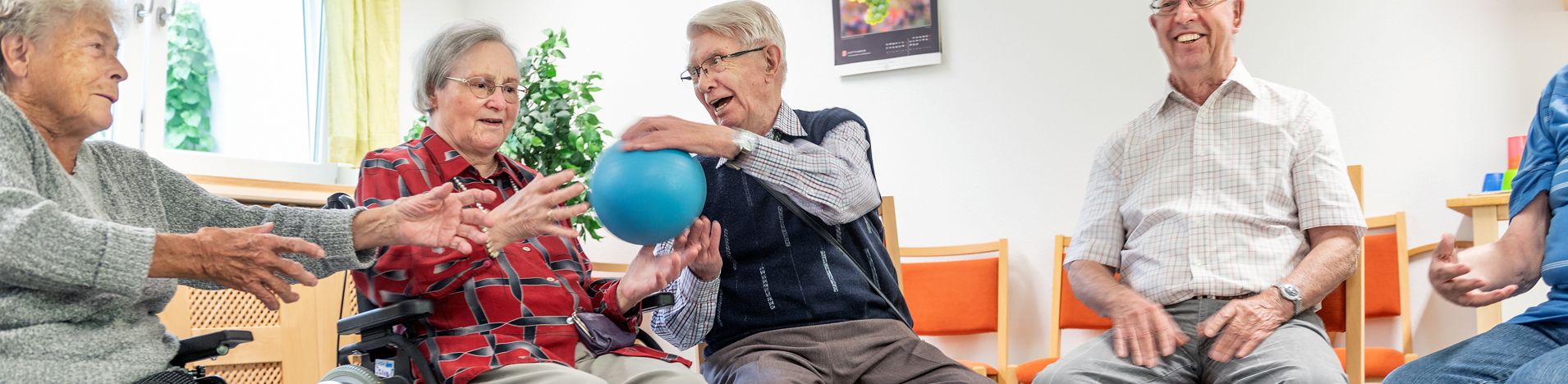 Ältere Menschen im Sitzkreis geben sich einen blauen Ball