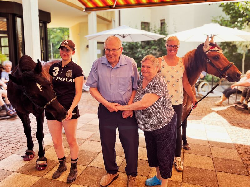 älteres Ehepaar auf einer Terrasse mit zwei Ponies mit Begleitung