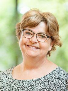 Lächelnde Frau mit Brille und gemustertem Oberteil vor grüner verschwommener Kulisse